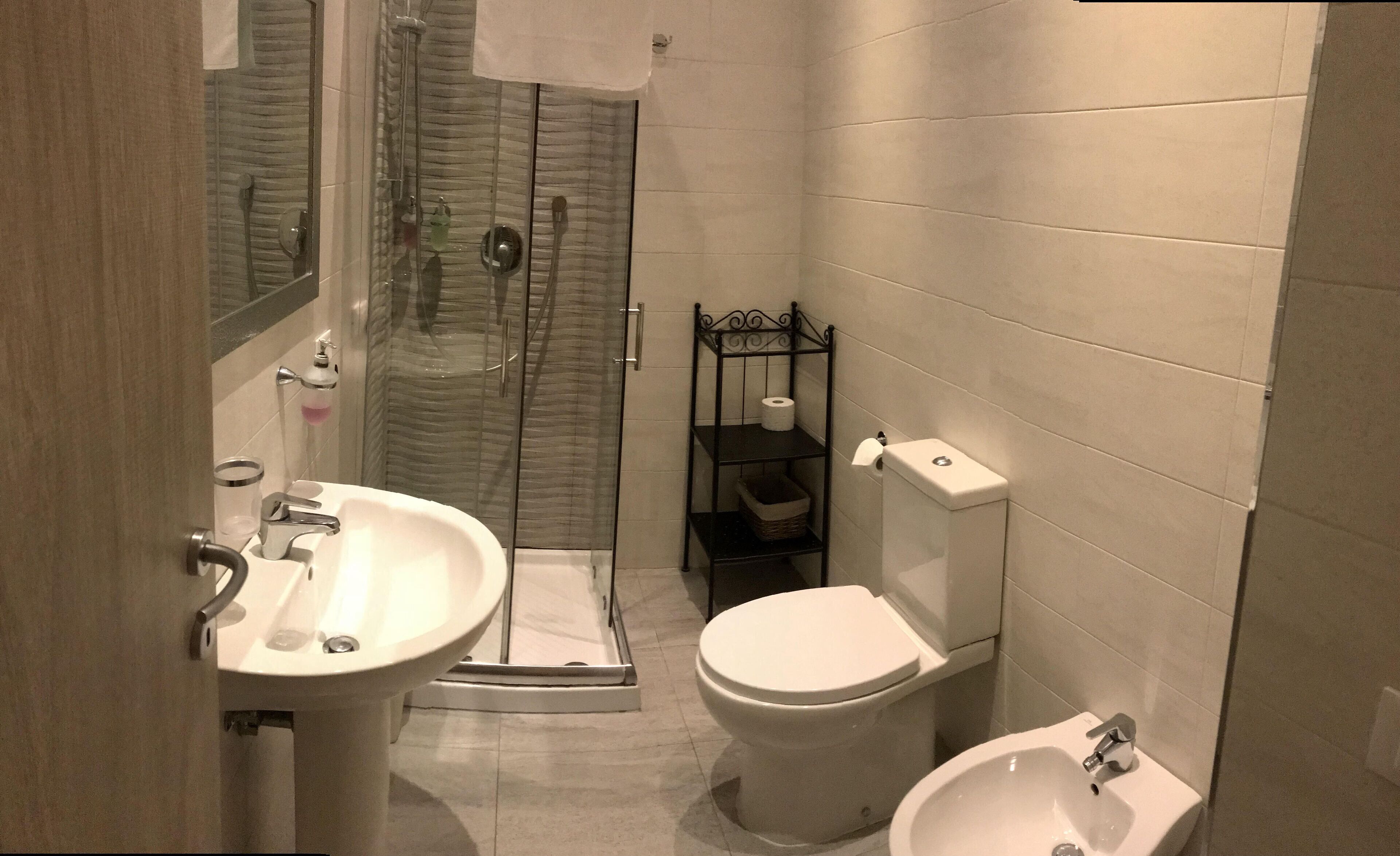 A bathroom with a glass shower enclosure, a pedestal sink, a toilet, and a bidet.