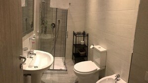 Un baño con cabina de ducha de vidrio, lavamanos pedestal, inodoro y bidé.