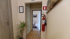 Un pasillo con suelo de madera, una planta en maceta, un extintor y una cama al fondo.