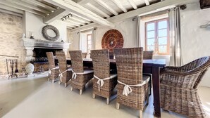 Un coin repas avec des chaises en osier, une cheminée et un mur en pierre.