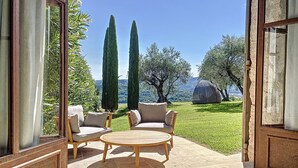 Une terrasse avec deux canapés et une table ronde, donnant sur un espace verdoyant agrémenté d’arbres et offrant une vue sur les collines.