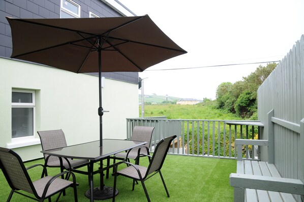 A patio with a table and chairs, an umbrella, and a view of a green landscape.