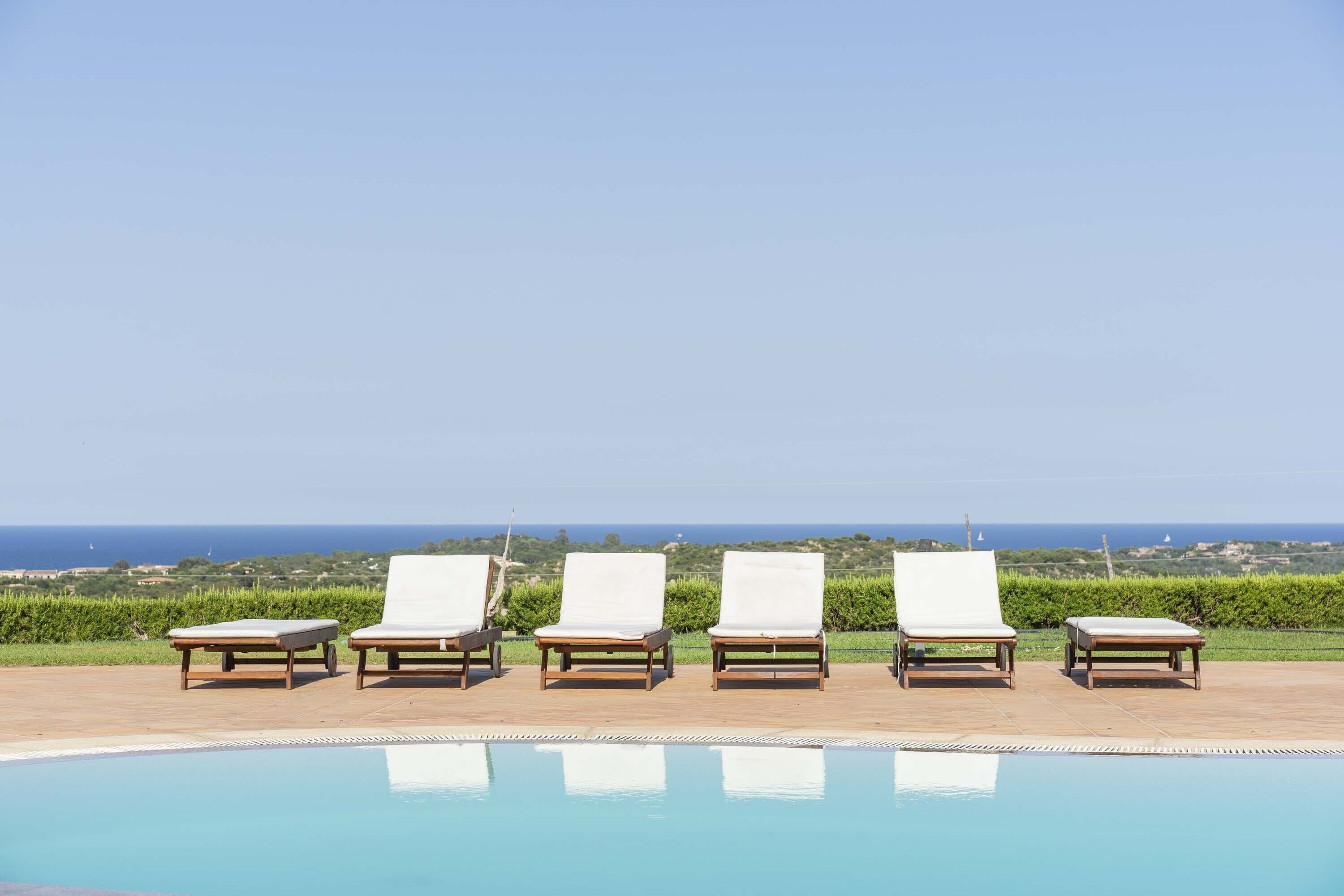 A poolside area with four lounge chairs and a clear view of the ocean.
