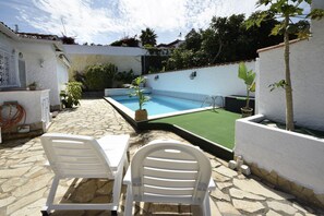 Area piscina con patio in pietra, due sedie in plastica bianca e un tavolino.