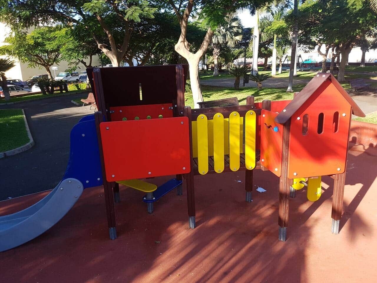 A playground with a slide, climbing structures, and a small house-like playhouse.
