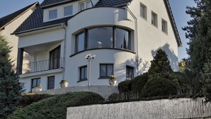 A modern two-story house with a curved balcony, large windows, and a tiled roof.