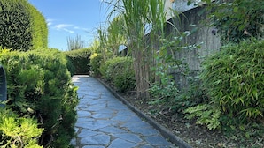 A stone pathway flanked by lush greenery and a building with a balcony.