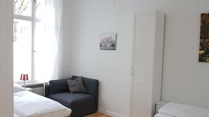 A room with two beds, a sofa, a chandelier, a radiator, and a window with curtains.