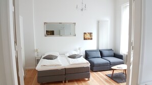 A modern bedroom with a double bed, a grey sofa, a small round table, and a large mirror.