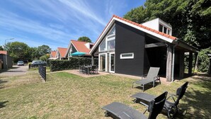 Una casa moderna con un amplio patio, mobiliario exterior y una zona cubierta.