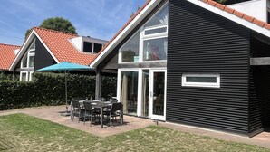 Una casa moderna con fachada negra, techo de tejas y un patio con mesa y sillas.