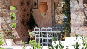 A rustic outdoor seating area with a stone wall, a wooden table, and chairs.