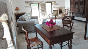 A rustic living room with a stone wall, a sofa, a wooden dining table with chairs, and a fireplace. - Character cottage **** Manor of Kerdanet Poullan sur Mer Sud Finistère Brittany (Poullan-sur-Mer)