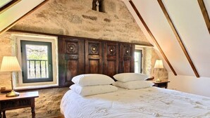 A bedroom with a sloped ceiling, wooden headboard, and a large bed with white bedding. - Character cottage **** Manor of Kerdanet Poullan sur Mer Sud Finistère Brittany (Poullan-sur-Mer)