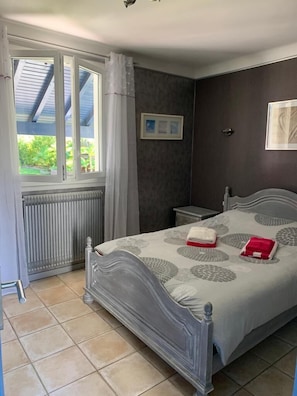 Um quarto com cama, mesa de cabeceira, janela com cortinas e radiador.