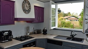 Una cocina con armarios morados, estufa a gas, cafetera y ventana con vistas a una casa y jardín.