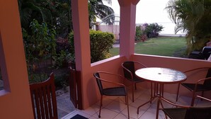 A covered outdoor seating area with a table and chairs, overlooking a well-maintained garden and a view of the sea. - Birdie's Nest condo #2 with ocean view (Black Rock)