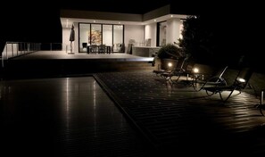 Relax by the pool with lounge chairs and a table, surrounded by large windows and lush greenery.