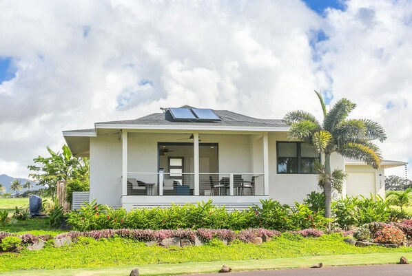 Una casa moderna de dos pisos con un porche cubierto, paneles solares y un jardín bien cuidado.