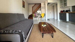 Un salon moderne avec un canapé, une table basse en bois et un escalier menant à un espace cuisine.