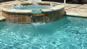 Zwembad met een jacuzzi, voorzien van een betegeld ontwerp en een fontein.