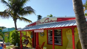 A small, brightly colored shoe gallery with a red and yellow facade, palm trees, and a sign reading "Merrell." - Sun, beach, and great savings –discover amazing discounts on dream destinations! (Cape Coral)