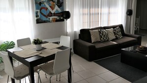 A modern living room with a dark brown sofa, white chairs, a dining table with placemats, and a large abstract painting on the wall. - Sun, beach, and great savings –discover amazing discounts on dream destinations! (Cape Coral)