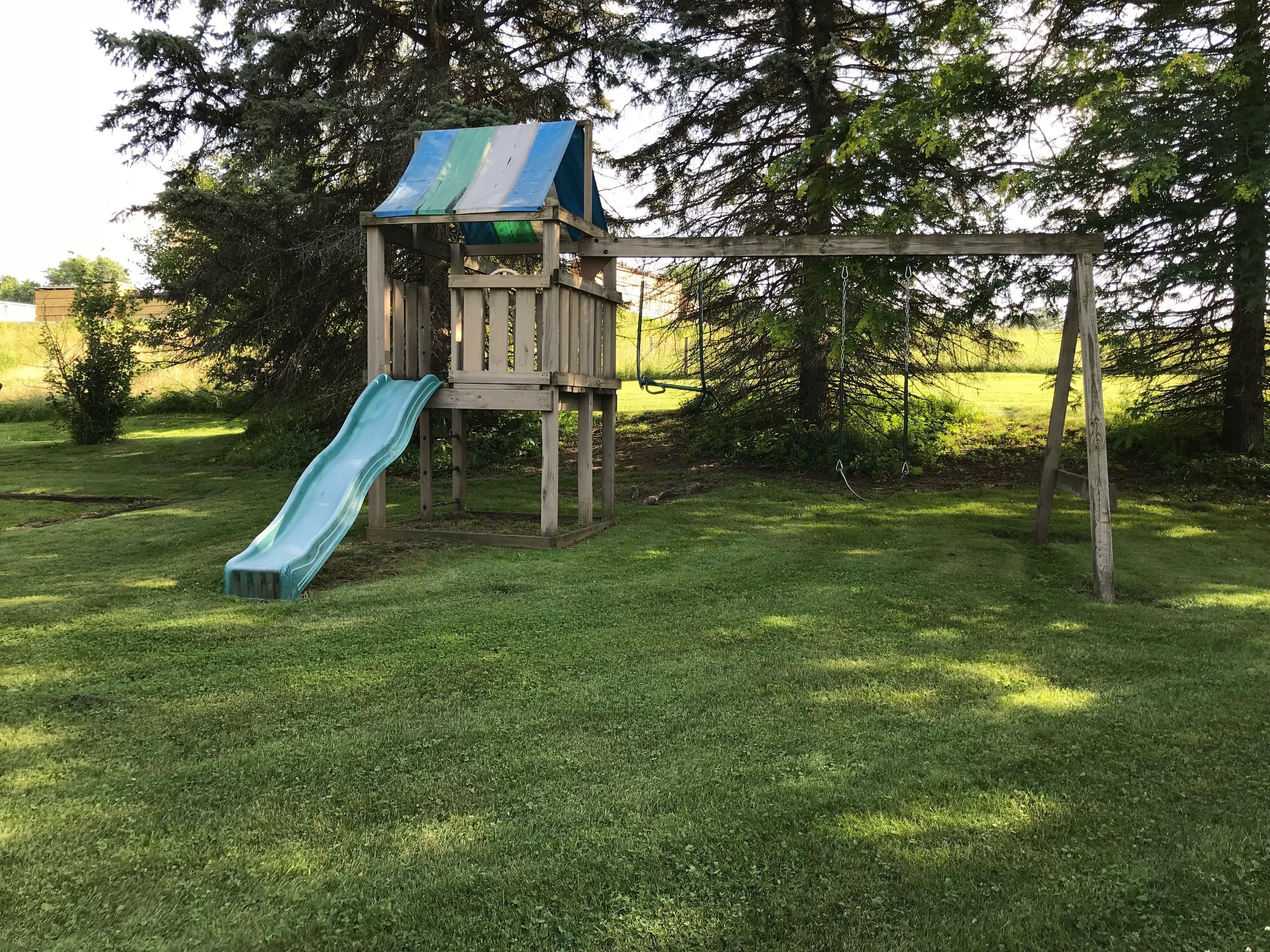 A wooden play structure with a slide and a swing set in a grassy yard.