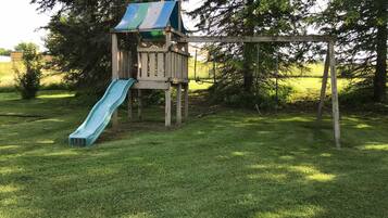 A wooden play structure with a slide and a swing set in a grassy yard.