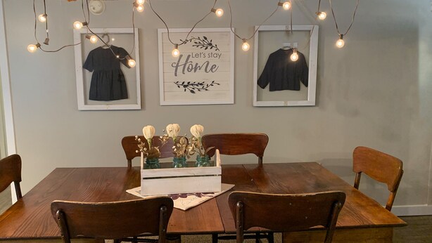 Un coin repas avec une table en bois, quatre chaises, des guirlandes lumineuses et des œuvres d’art encadrées accrochées au mur.