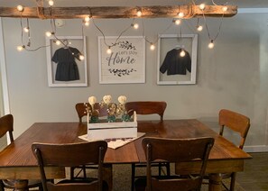 Un coin repas avec une table en bois, quatre chaises, des guirlandes lumineuses et des œuvres d’art encadrées accrochées au mur.