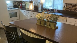 Une cuisine avec des meubles blancs, un four à micro-ondes, une cuisinière et un îlot central en bois avec des chaises.