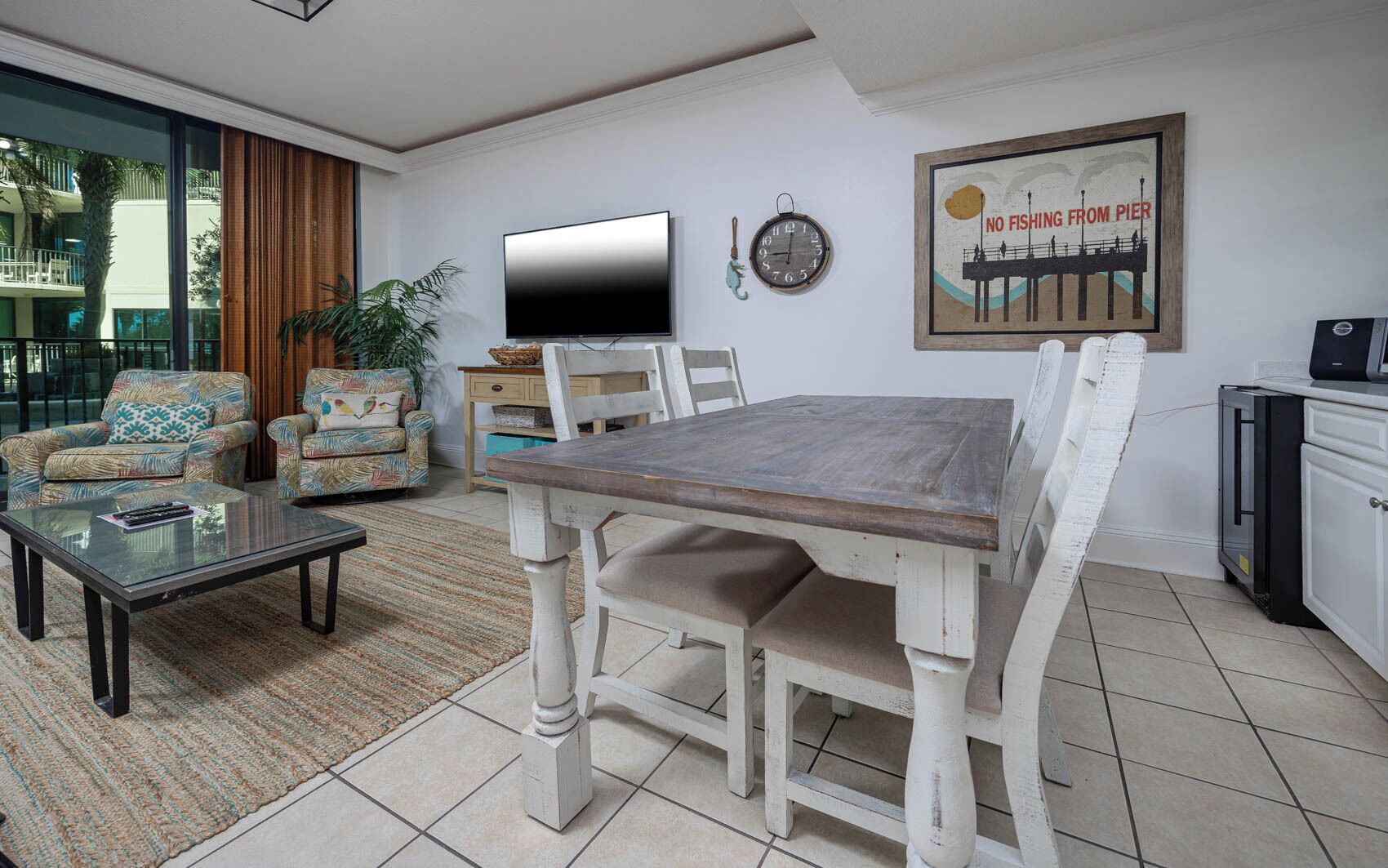 A living room with a wooden dining table, two armchairs, a sofa, a TV, and a clock on the wall.