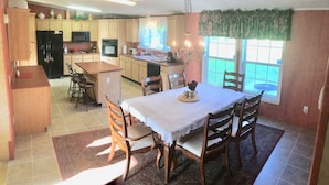 A spacious kitchen with wooden cabinets, a dining area with a table and chairs, and a large window providing natural light. - Sleeps 6 in 4 Queen Beds, former farmland, near New Bern, home of Tryon Palace. (New Bern)