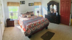 A bedroom with a large bed, a dresser, a mirror, and a door. - Sleeps 6 in 4 Queen Beds, former farmland, near New Bern, home of Tryon Palace. (New Bern)