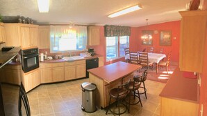 A kitchen with wooden cabinets, a stove, a sink, and a dining area with chairs and a table. - Sleeps 6 in 4 Queen Beds, former farmland, near New Bern, home of Tryon Palace. (New Bern)
