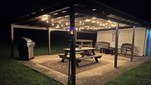 Un espace extérieur aménagé en terrasse, avec une table de pique-nique, des bancs et des guirlandes lumineuses.