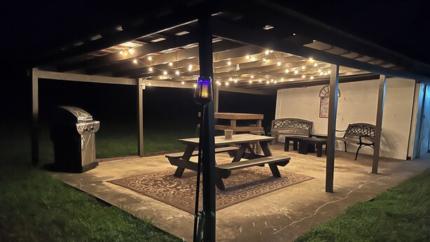 An outdoor patio area with a picnic table, benches, and string lights. - Sleeps 6 in 4 Queen Beds, former farmland, near New Bern, home of Tryon Palace. (New Bern)