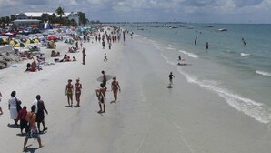 A crowded beach with people walking and swimming, umbrellas, and boats in the water. - Sun, beach, and great savings –discover amazing discounts on dream destinations! (Cape Coral)