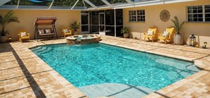 Une piscine avec un jacuzzi, entourée de chaises de patio et de plantes en pot.