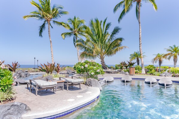 Relax by the serene pool surrounded by lounge chairs, umbrellas, and lush tropical plants.