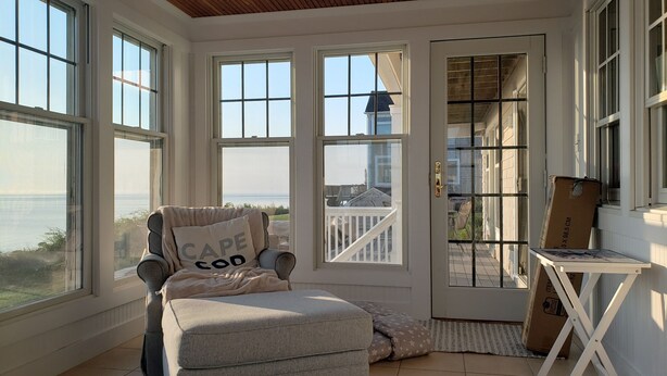 Habitación soleada con vista al mar, un sillón acolchado con un cojín y una mesita con una caja.