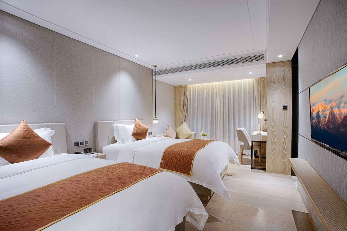 A hotel room with two beds, a desk, a chair, a TV, and a curtain.