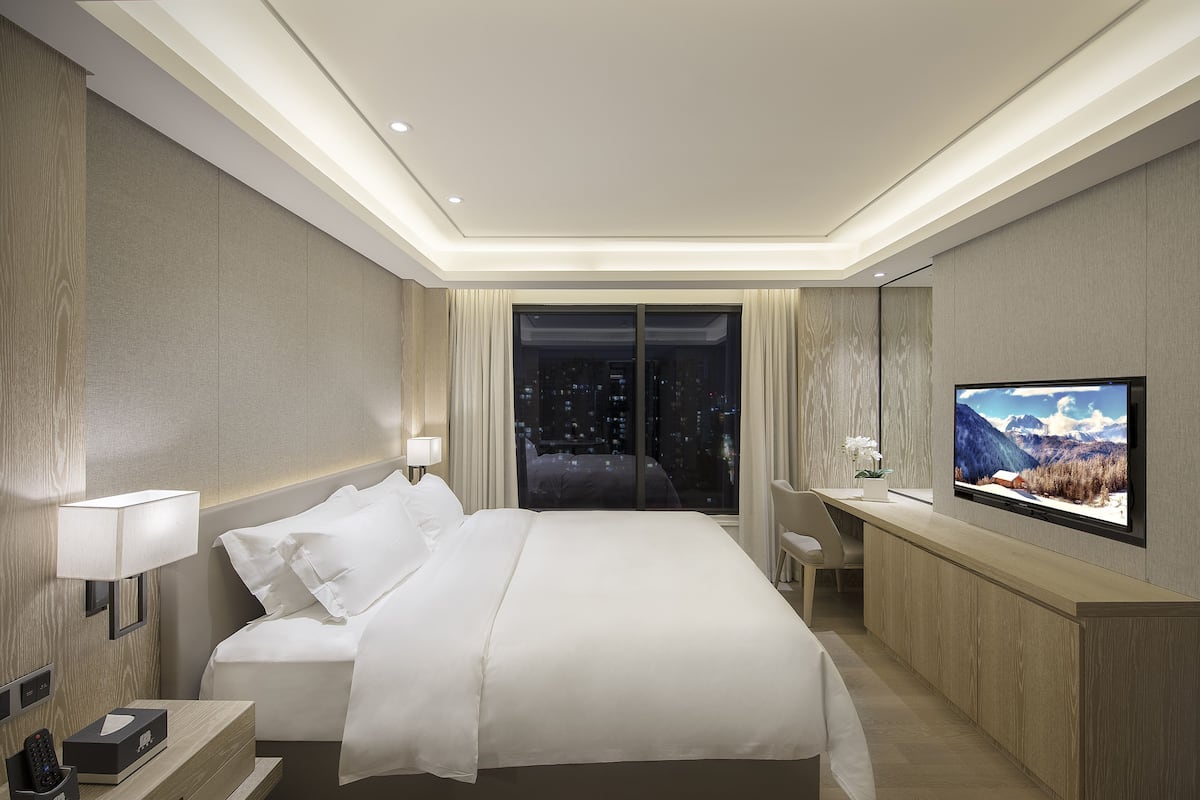 A modern hotel room with a large bed, a TV, and a city view.