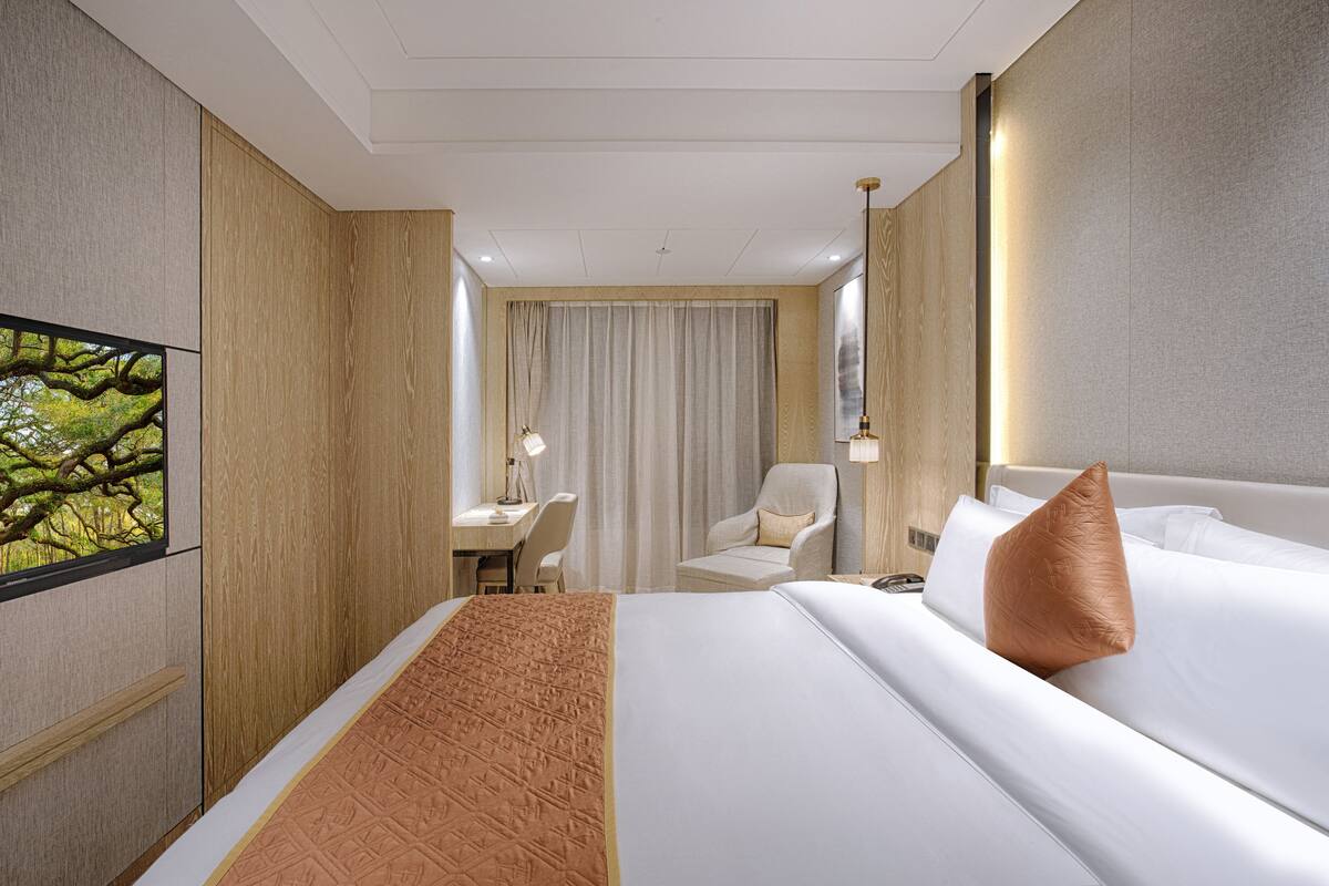 A hotel room with a large bed, a desk, a chair, and a TV on the wall.