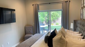 A hotel room with a bed, a chair, a TV, and a view of the outdoors. - Pool Side Villa |Pet-Friendly Modern Escape w/ Games, Pool Toys, Bikes & More! Near St.George (Washington)
