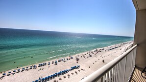 A beach with a clear view of the ocean, a pier in the distance, and a balcony overlooking the beach.