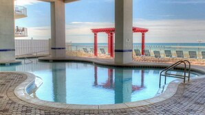 An indoor swimming pool with a view of the beach and a red pavilion.
