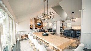 A spacious kitchen with a large island, modern bar stools, and a dining area with a long wooden table and white chairs.
