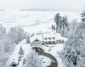 A large house with a snow-covered driveway and a pond in the background. -  ADIRONDACK LUXURY LAKE ESTATE: POOL & HOT TUB! NEWLY RENOVATED! (Remsen)